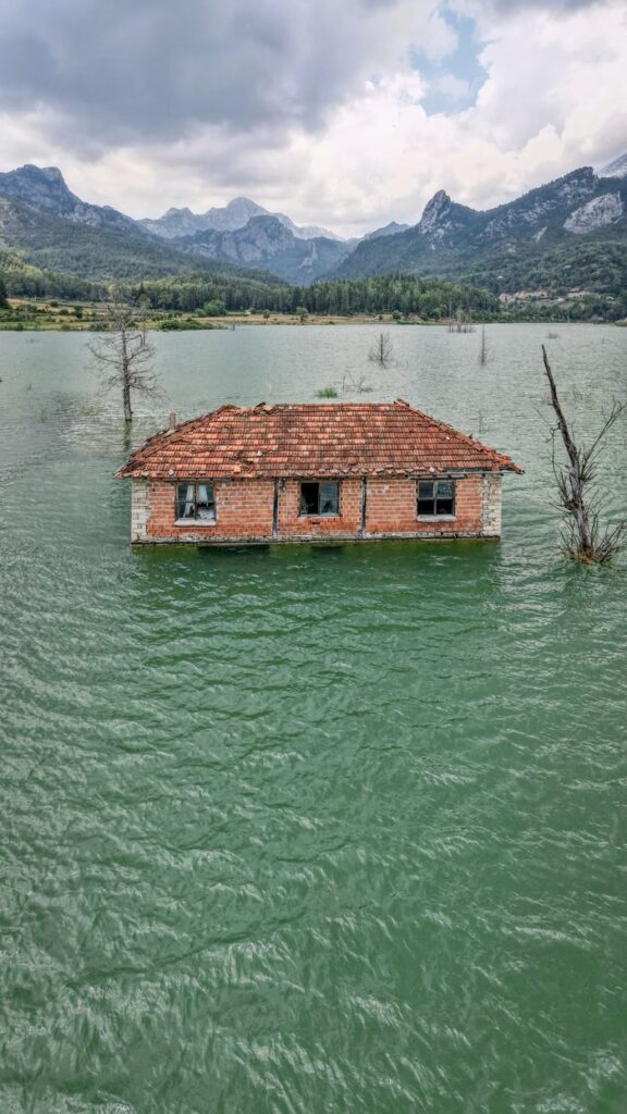 An abandoned house partially submerged in a serene lake surrounded by mountains in Serik, Antalya.